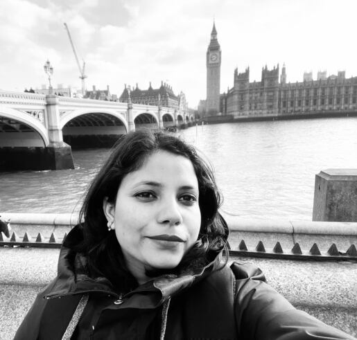 Woman in a coat taking a selfie by the River Thames with Big Ben and Westminster Bridge in the background.