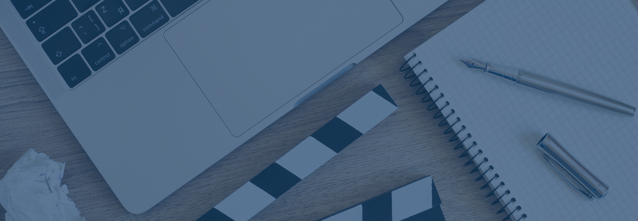 Laptop keyboard, notebook with pen, and a Hollywood clapperboard on a wooden surface.