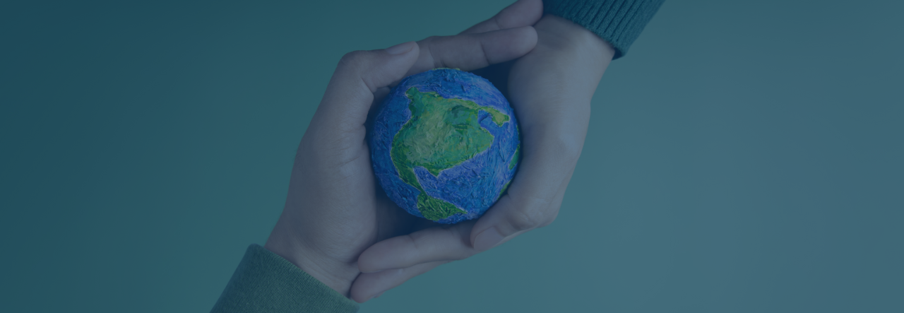 Hands holding a small Earth model with visible continents against a blue background.