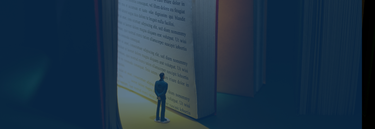 A small figurine of a man stands in front of a large open book illuminated by soft light.