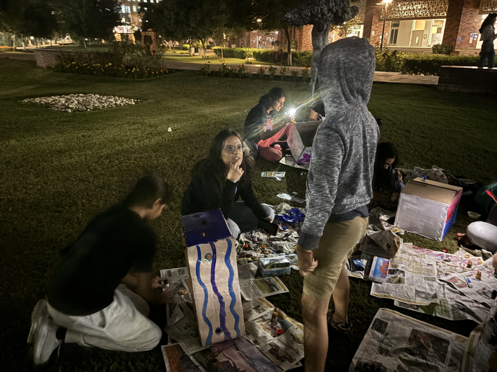 People crafting and painting outdoors at night, surrounded by newspapers and art supplies.