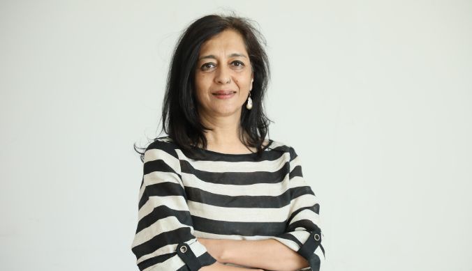 Woman with long black hair wearing a black-and-white striped top, standing with arms crossed.