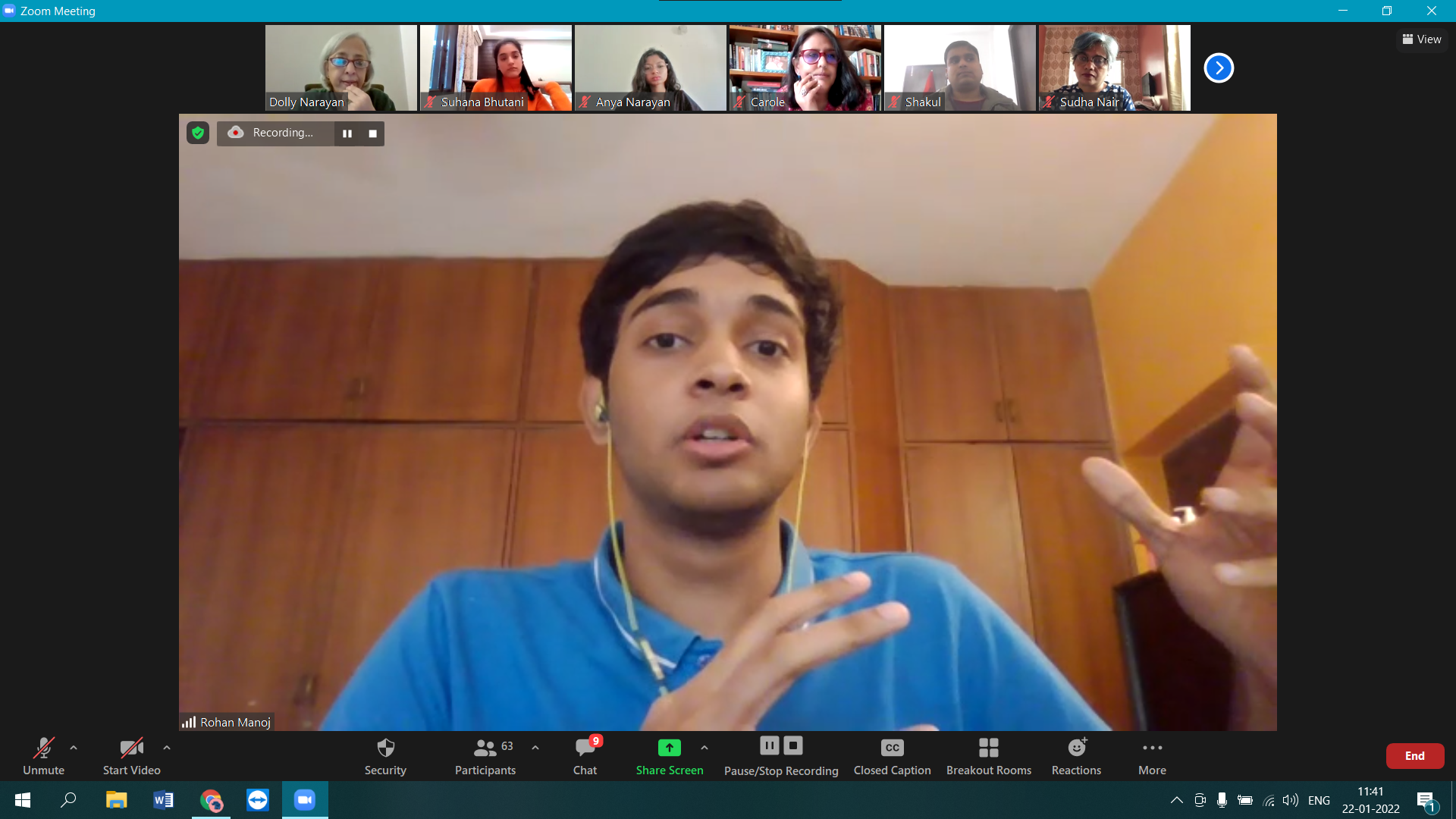 Person in a blue shirt speaking during a Zoom meeting, with six participants visible in the top bar.