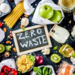 Zero waste written on a chalkboard surrounded by fresh produce, pasta, grains, and reusable containers.