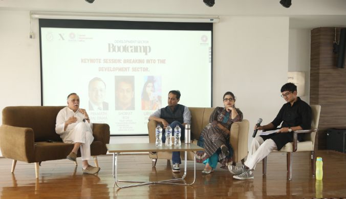 Panel discussion with four speakers seated on a stage, projector screen in the background.