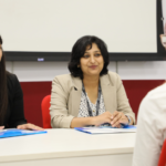 Two women conducting an interview at a table, facing a candidate with red hair in a white shirt.