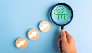 Hand holding magnifying glass over CO2 cloud icon, three wooden circles with white arrows below.