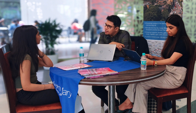 Three people seated at a table with laptops and brochures, engaged in a discussion indoors.
