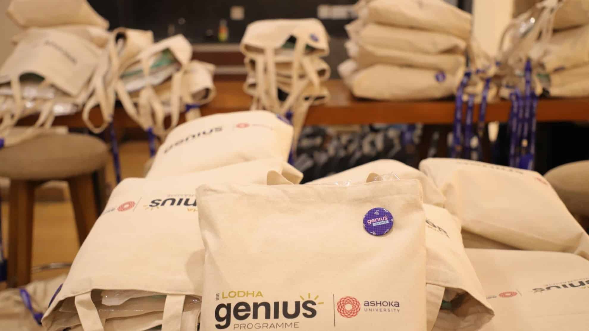 Canvas tote bags with "Lodha Genius Programme" and "Ashoka University" logos stacked on a table.