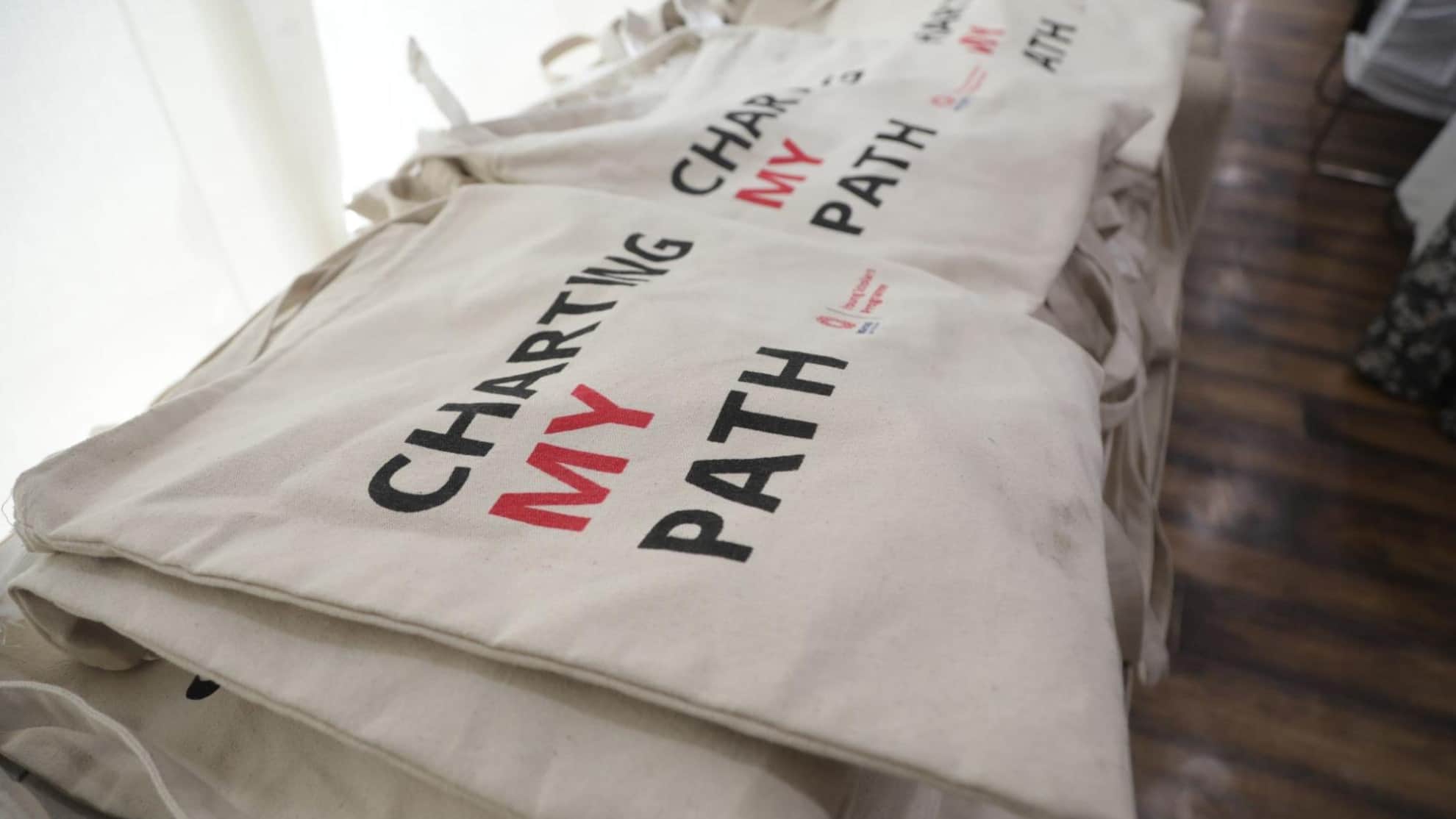 Canvas tote bags stacked, featuring the text "Charting My Path" in bold black and red lettering.