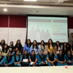 Group of women and girls posing in a classroom with a presentation screen in the background.
