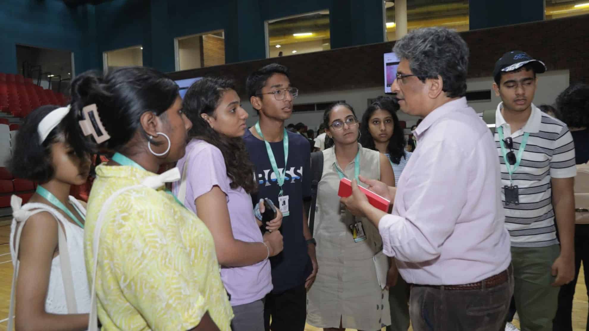 A group of students listens attentively to a man holding a red object in a well-lit indoor space.