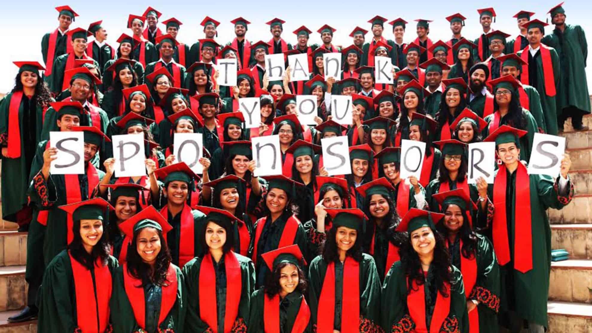 Graduates in green robes and red stoles holding signs reading "Thank You Sponsors" on steps.