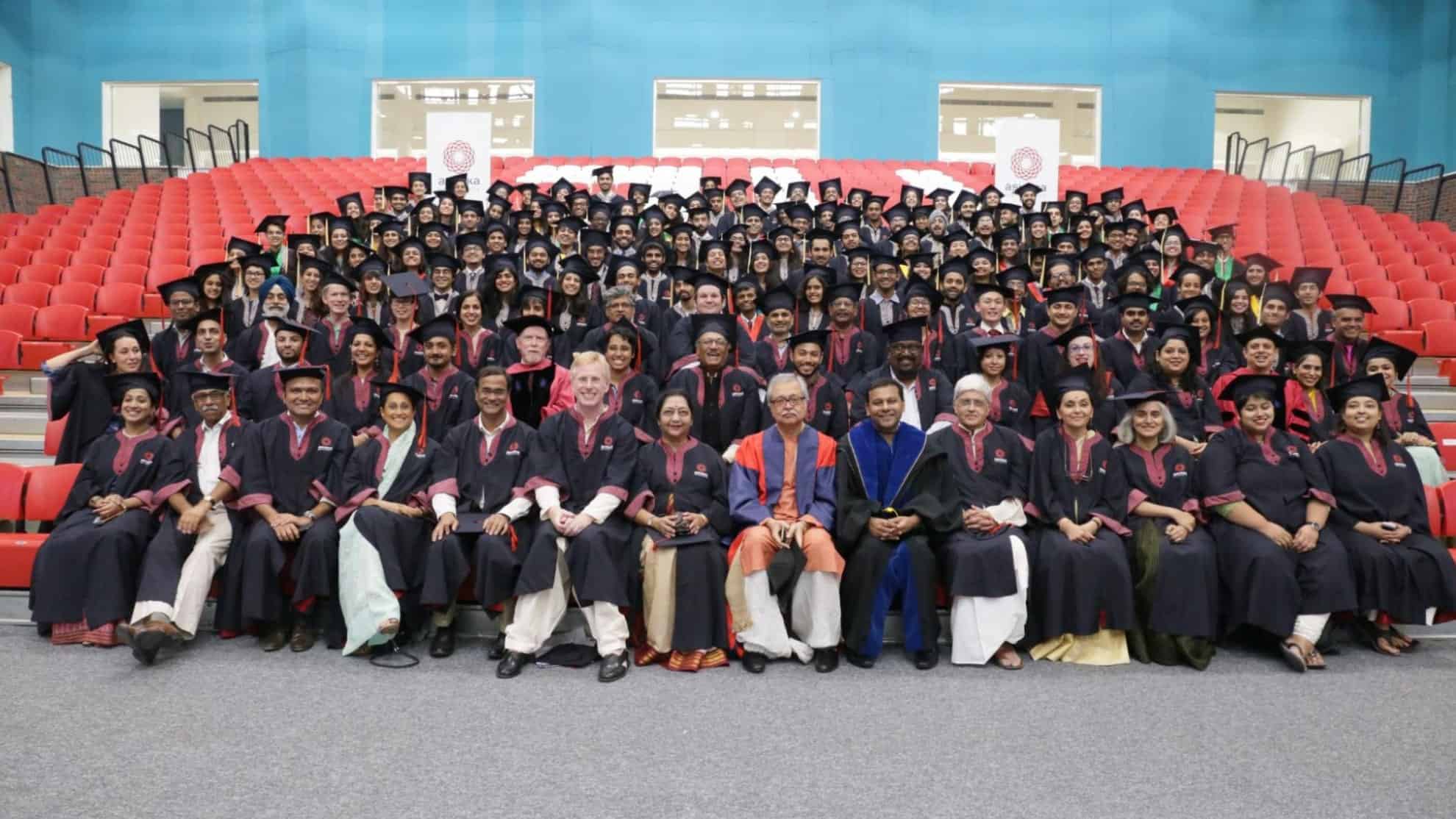 Graduates and faculty in academic robes seated and standing in rows in an auditorium.