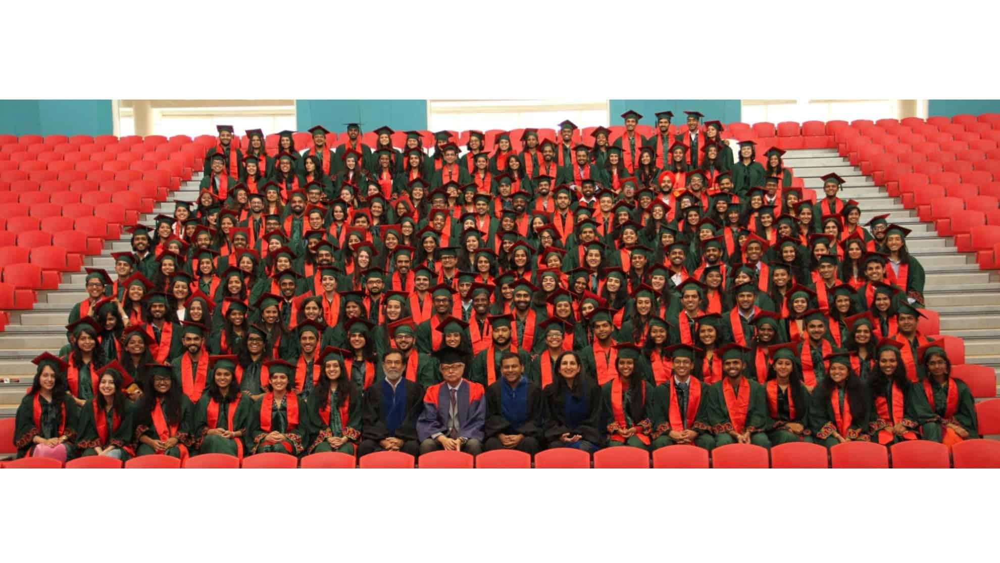 Graduation group in green gowns and red stoles seated in rows with faculty in front.