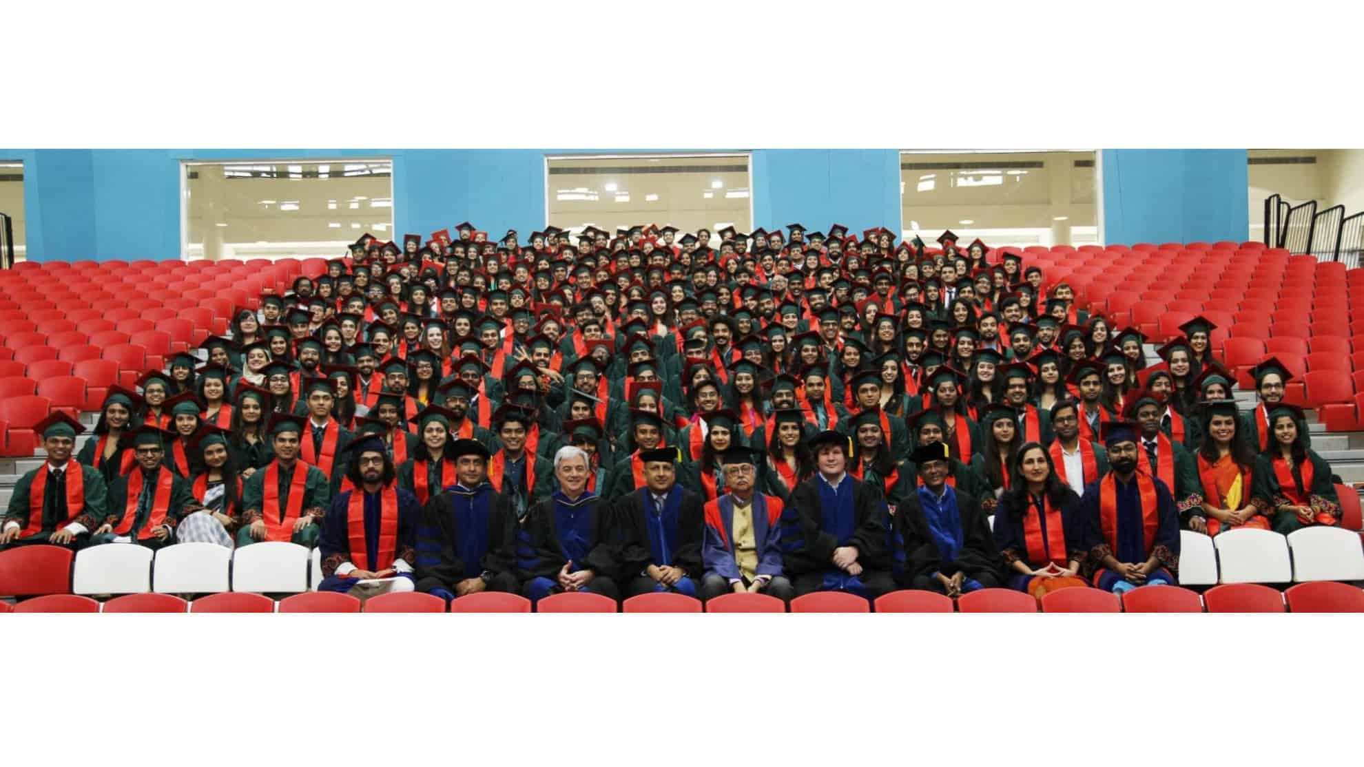 Graduates in caps and gowns with orange stoles seated in rows, faculty seated in front.