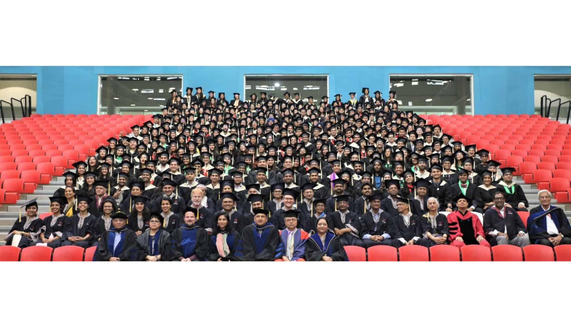 Graduating students and faculty seated in rows with caps and gowns in an auditorium.