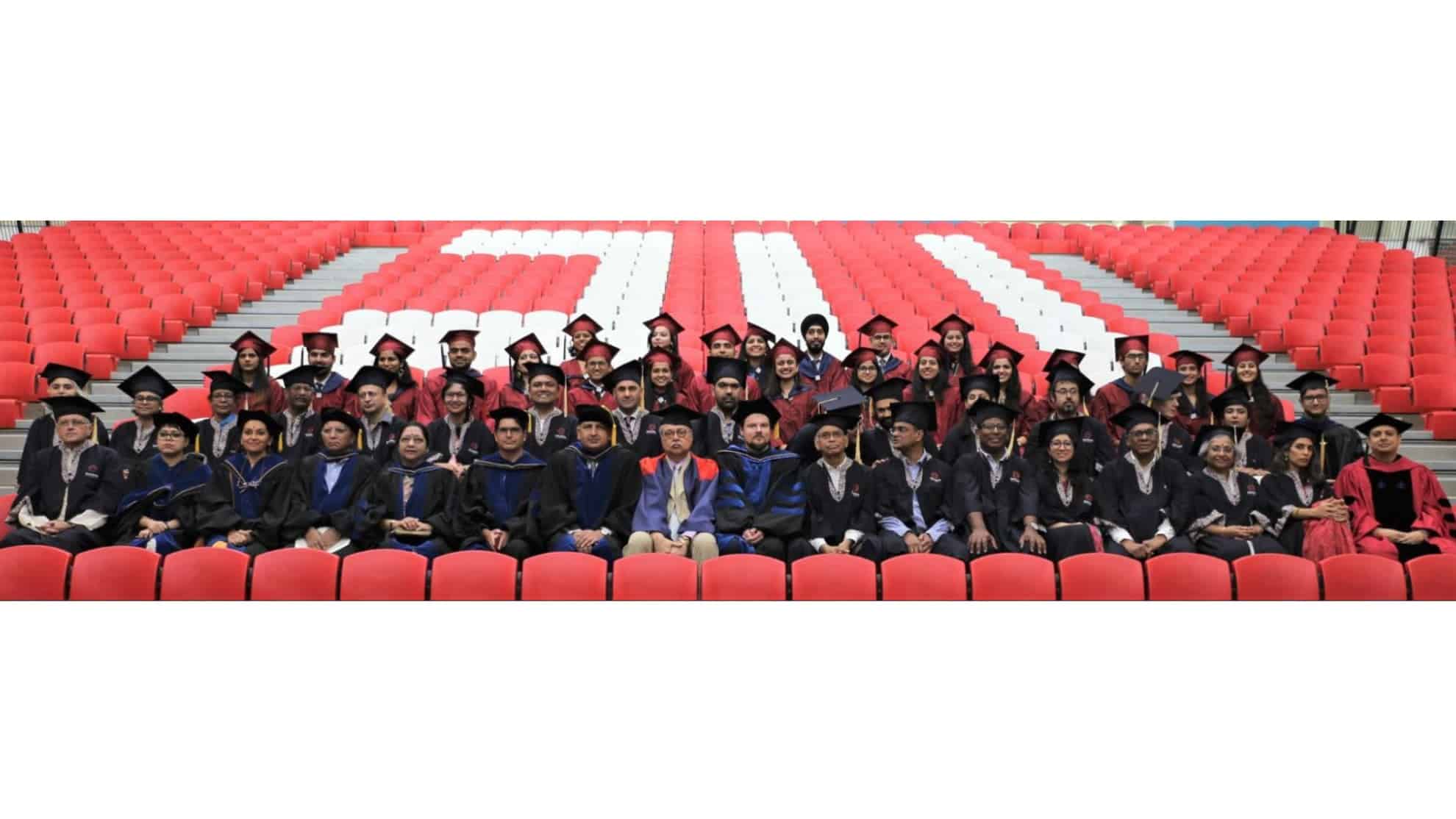 Graduates and faculty in academic regalia seated in rows with red and white chairs in the background.