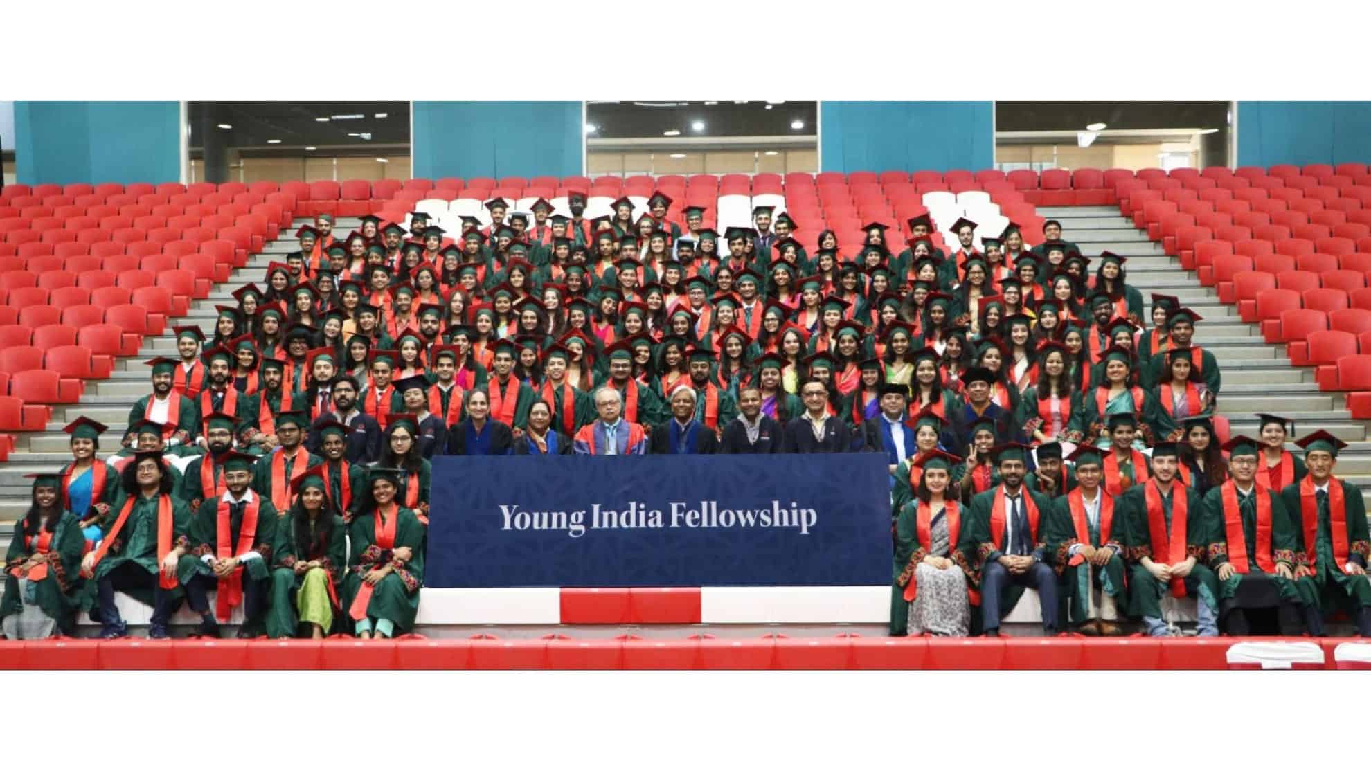 Graduates in green robes with orange stoles seated in rows, Young India Fellowship banner in front.
