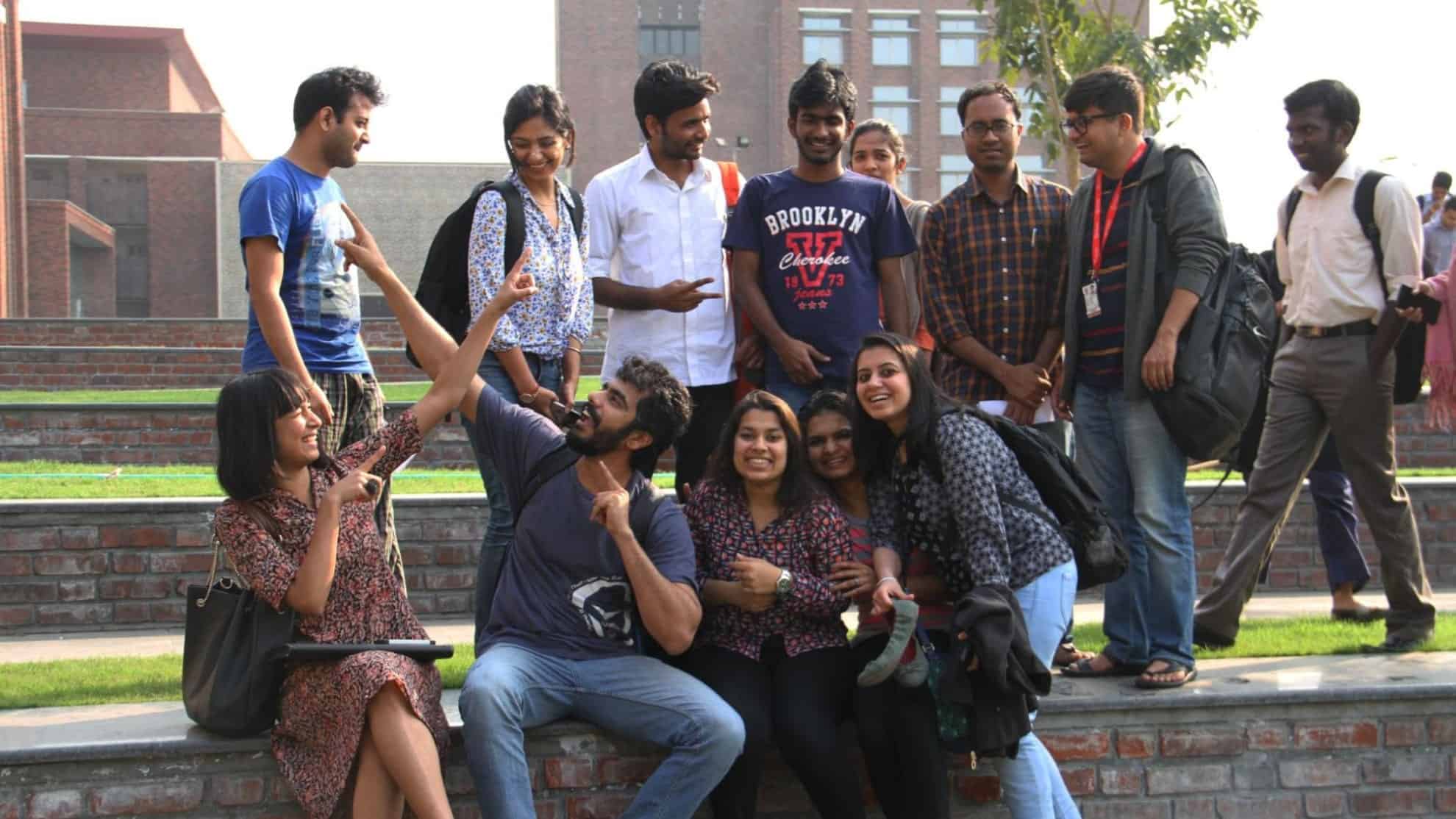 Group of students laughing and posing together outdoors on a sunny day near brick steps.