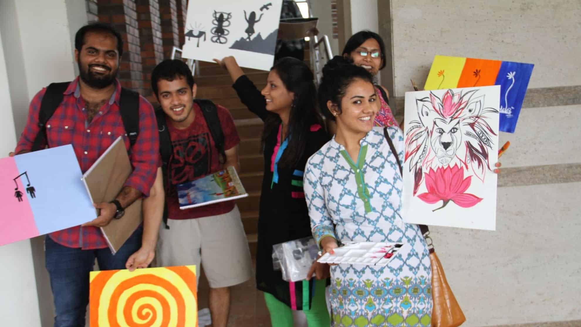 Group of smiling people holding colorful artwork, including a lion drawing and abstract designs.