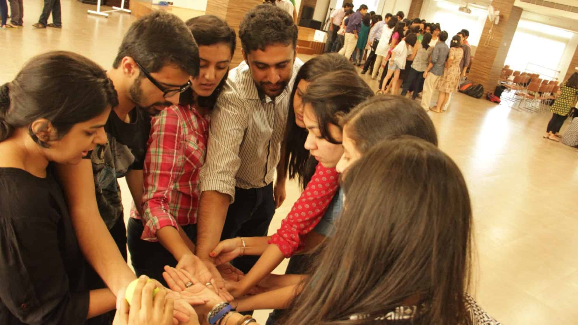 A group of people standing in a circle, stacking their hands together in a bright indoor space.
