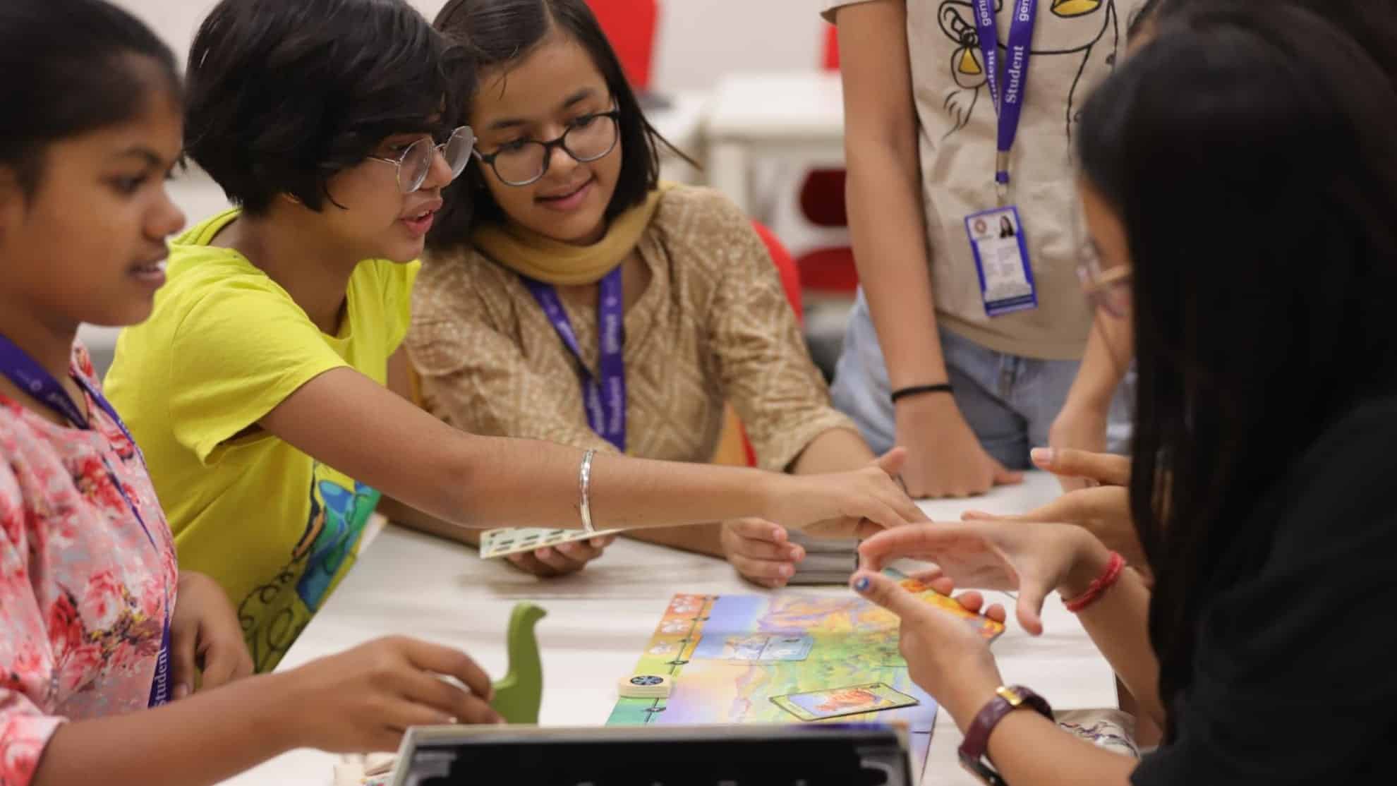 Group of students playing a board game, engaging in discussion, and handling game pieces.