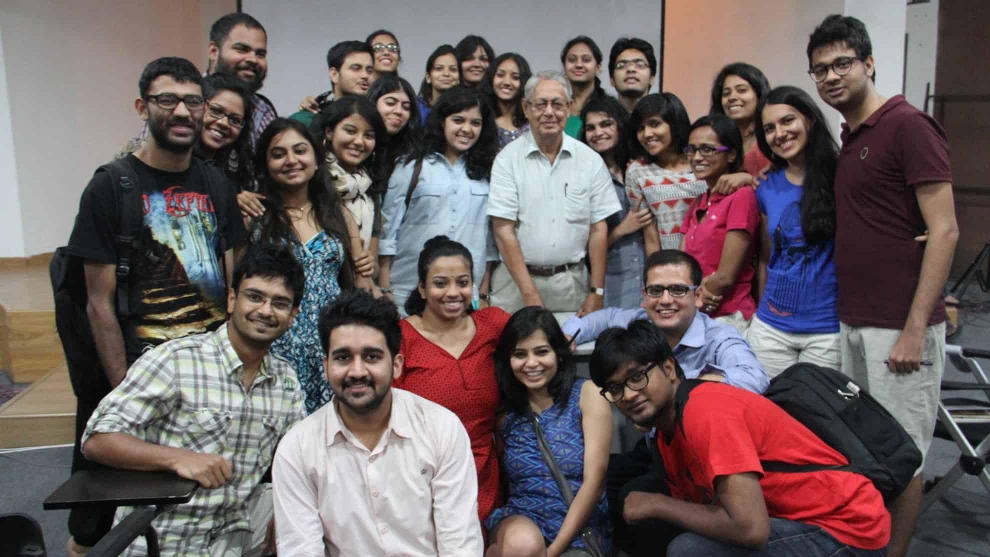 Group of smiling people, including a man in a white shirt, gathered indoors in a casual setting.