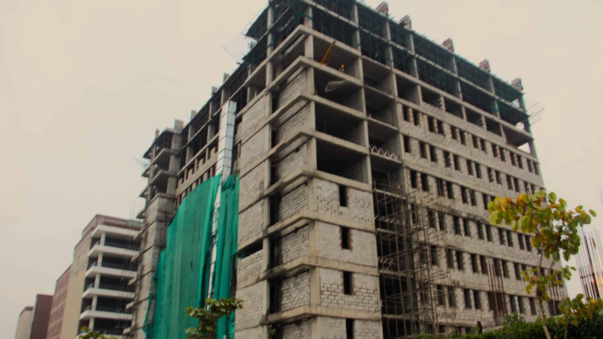 Unfinished multi-story building with exposed concrete, scaffolding, and green covering material.