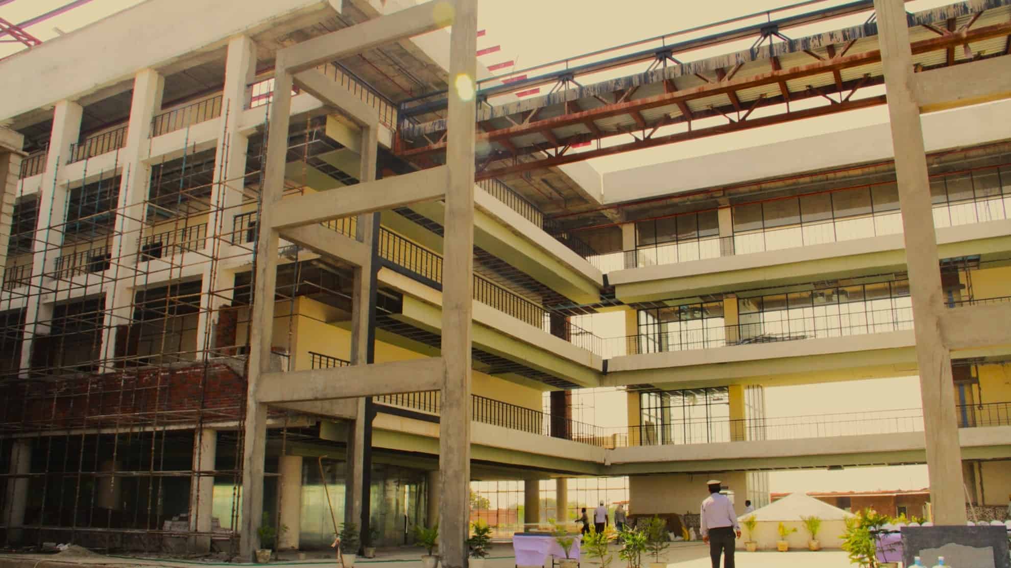 Unfinished multi-story building with scaffolding, glass windows, and a man in a hat standing nearby.