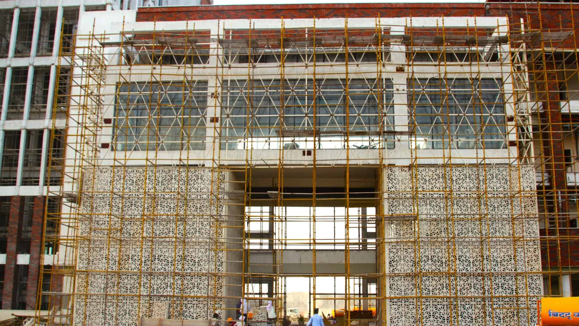 Building under construction with intricate facade, glass windows, and bamboo scaffolding.