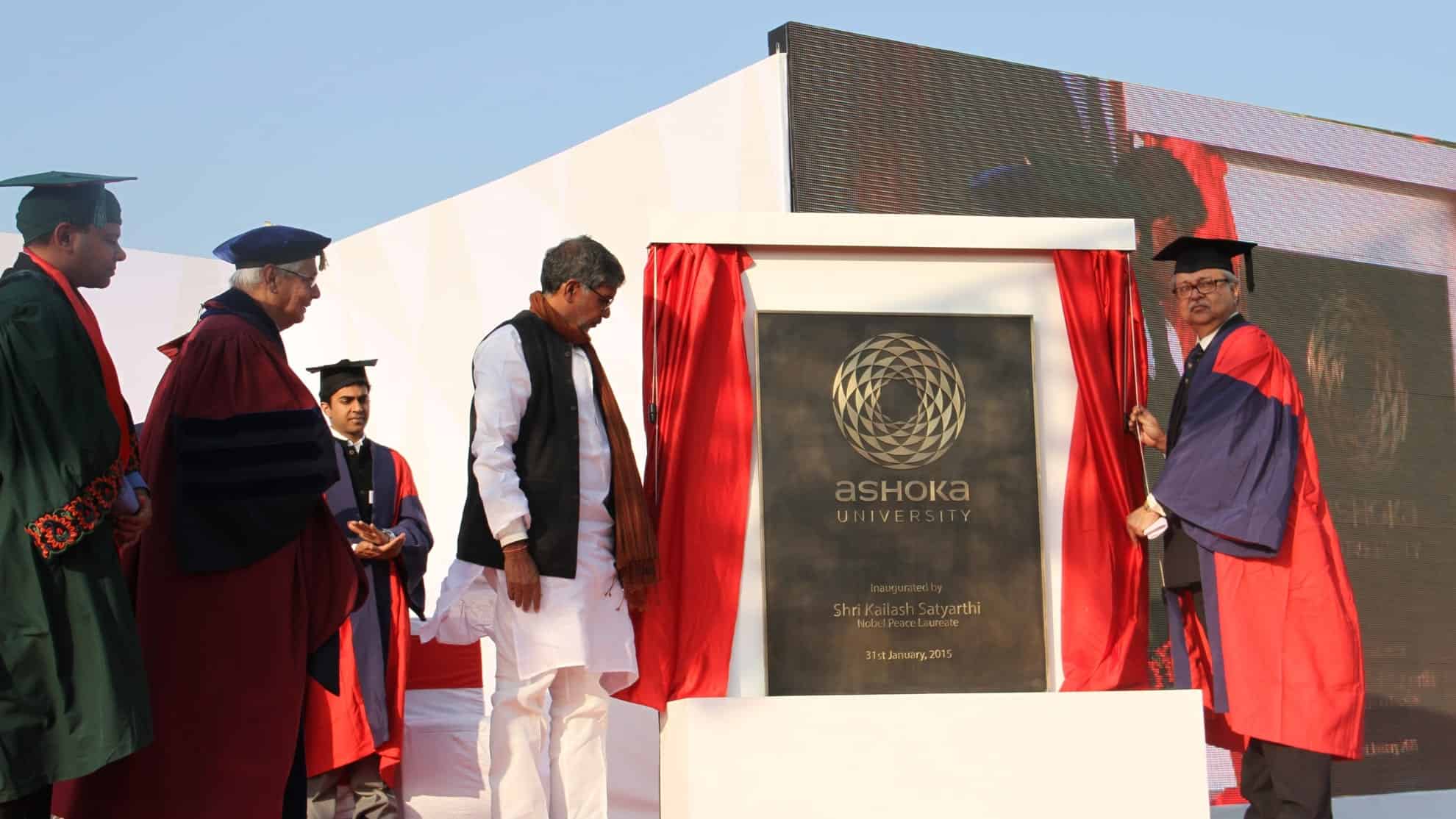 Group unveiling Ashoka University plaque, featuring people in academic robes and formal attire.