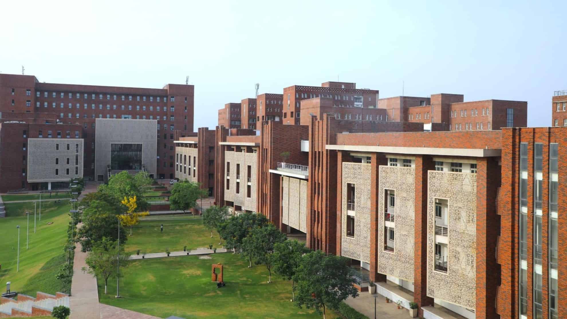 Red-brick campus buildings with large windows, green lawns, trees, and pathways in the foreground.