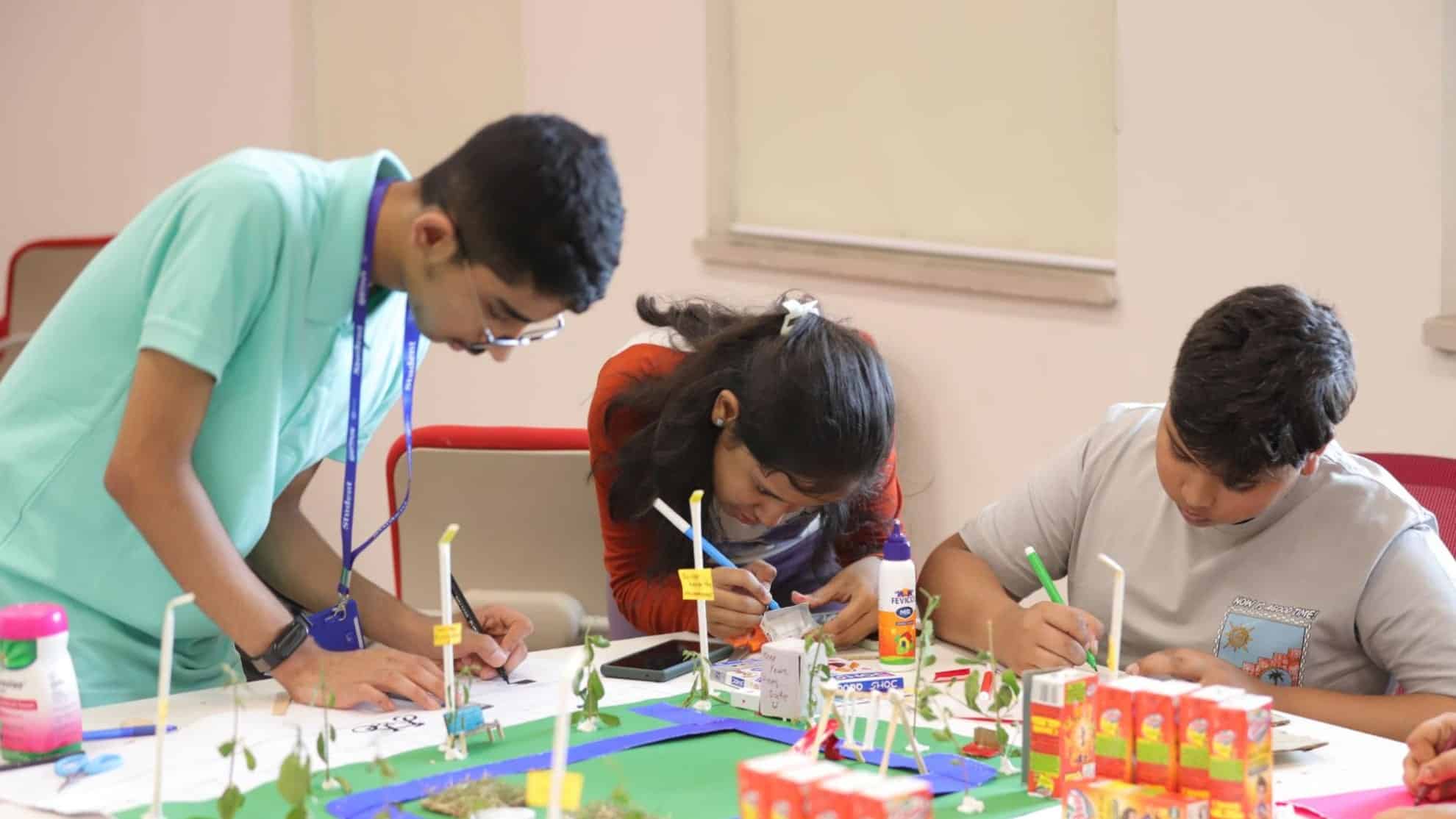Three students working on a creative project with craft materials and a model on a table.