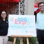 Two people standing next to an SDG Expo sign with red tents and event booths in the background.