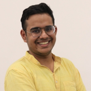 Smiling person wearing glasses and a yellow shirt against a plain light background.