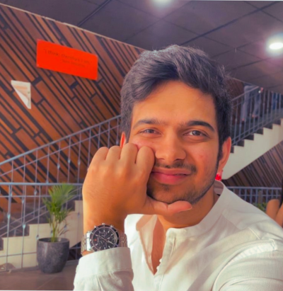 Man in a white shirt smiling, resting his chin on his hand, staircase and plants in the background.