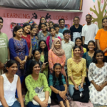 Group of smiling people in a colorful room with "Learning Locals" written on the back wall.
