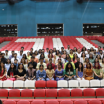 Group of people seated in rows, with red and white stadium seats