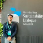Man standing in front of a Mercedes-Benz Sustainability Dialogue India 2024 sign, surrounded by plants.