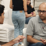 Two men engaged in a serious discussion, with two women chatting in the background.