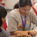Two students work together on an electronics project with wires and components on a table.