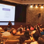 Speaker presenting degree requirements to an audience in a lecture hall with a projected slide.