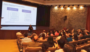 Speaker presenting degree requirements to an audience in a lecture hall with a projected slide.
