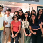 A group of young people smiling, standing indoors with a menu board visible in the background.