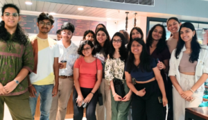A group of young people smiling, standing indoors with a menu board visible in the background.