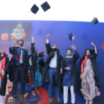 Graduates in caps and gowns celebrate by tossing caps in the air, standing in front of a colorful wall.