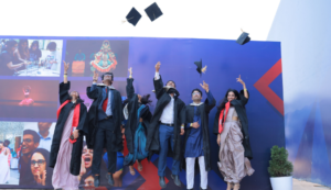Graduates in caps and gowns celebrate by tossing caps in the air, standing in front of a colorful wall.