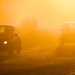 Cars driving on a dusty road at sunset with golden light and shadows.