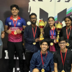 A group of smiling young adults with medals and trophies, posing in front of a sports-themed backdrop.